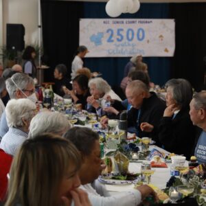 photo of the group sitting at tables enjoying lunch with a banner int he background displaying 2500 walks.