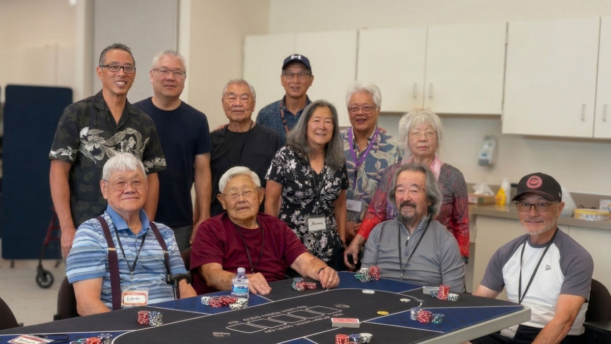 Eleven older adults pose and smile around a blue poker table with chips and cards. Some are seated, others stand behind, in a bright room with white cabinets.